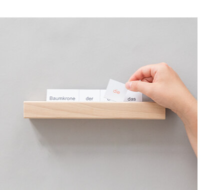 Eine Hand steckt beschriftete Papierkarten in eine waagerechte Einkerbung auf einer Holzleiste.