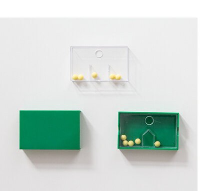 Das Set besteht aus einer grünen, aufschiebbaren Hülle aus Kunststoff, einem durchsichtigen Inlay und kleinen Kugeln, die durch ein Hindernnis getrennt werden können.