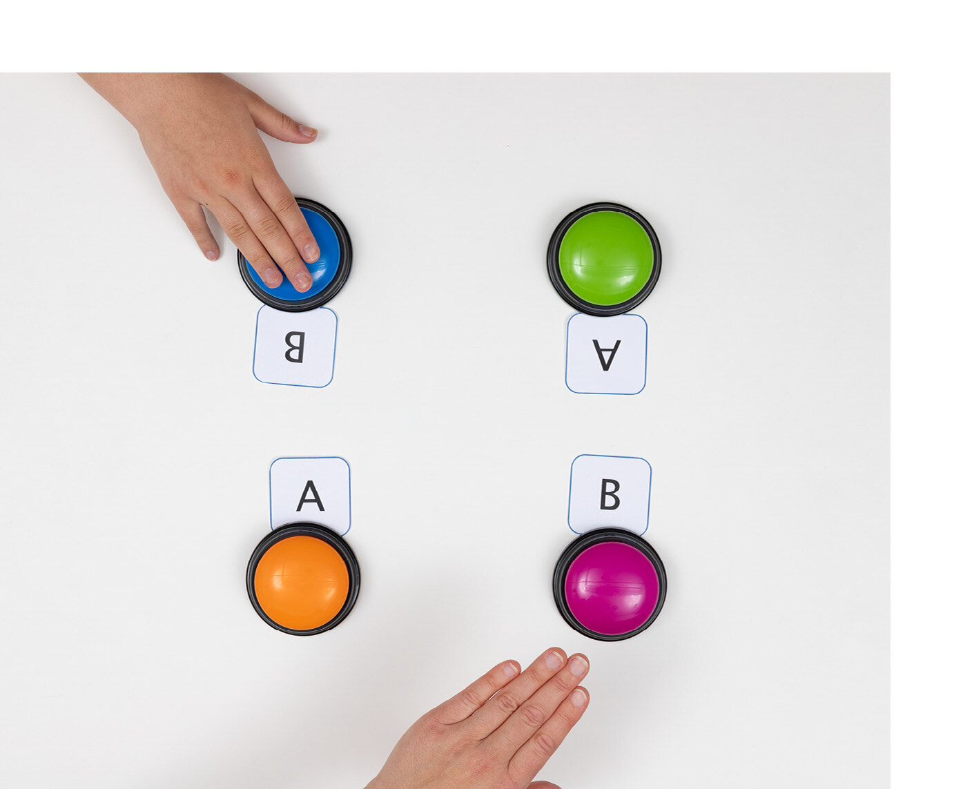 Vier unterschiedlich farbige Buzzer liegen zu einem Viereck angeordnet. An Jedem Buzzer liegt eine Karte, auf der ein A oder ein B steht.