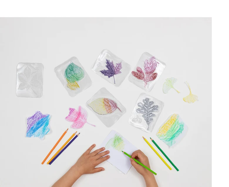 Ein Blatt Papier liegt über einer Kunststoffplatte und jemand malt mir einem bunten Stift über die Kunststoffplatte, sodass die Strukturen eines Blattes sichtbar werden.