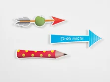 Ein Pfeil, der einen Apfel aufspießt, ein Pfeil, auf dem steht: "Dreh mich!" und ein roter Bundstift mit gelben Punkten zeigen nach rechts.