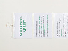 Zwei beschriebene Notizblätter stecken unter einander angeordnet in einer Plastikhülle. Diese Plastikhülle ist an einem Kleiderbügel befestigt.